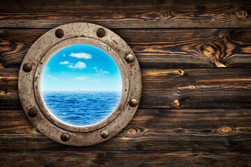 Close-up of an old rusty closed porthole window with  ocean and blue sky view. Old rich wood grain texture background with knots.