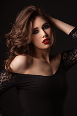 Naklejka premium Beautiful bright makeup woman with long brown curly volume hair style, red lipstick, and black smokey eyes looking vamp and passion on black background. Closeup