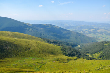Lush green grassy meadows on the mountain slopes on background of blue sky. Beautiful landscape of...