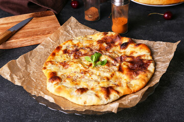 Parchment with tasty khachapuri on dark background