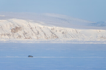 Winter Arctic landscape. The car is driving on snow and ice. Winter ice road along the frozen river. Extreme travel and car trips in the Arctic. Anadyr estuary, Chukotka, Siberia, Far North of Russia.