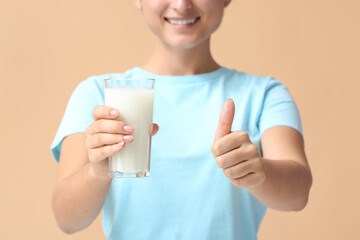 Young woman with glass of organic milk showing thumb-up gesture on color background, closeup