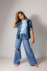 young curly haired woman with blue eyes in a full length denim suit. model poses in the studio. space for text. High quality photo