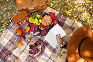 Woman reading book during romantic picnic in park, top view