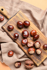 Wooden board with chestnuts on color background, closeup