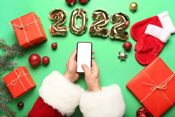 Santa Claus with mobile phone and balloons in shape of figure 2022 on green background