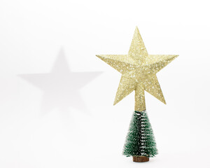Gold shiny star ornament on the top of Christmas tree.  Minimal festive New Year concept for holidays on white background.