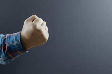 Male hand in a checkered sleeve clenched into a fist on a gray background. A harsh gesture....