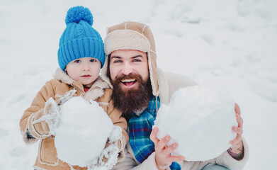 Winter, father and baby son play outdoor. Happy father and son making snowman in the snow. Handmade funny snow man.