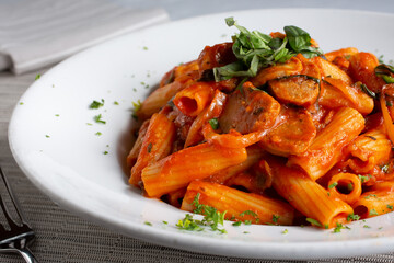 A view of a plate of rigatoni pasta with sausage, in a restaurant or kitchen setting.