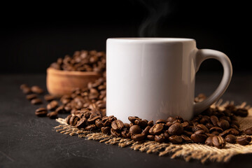 White lungo cup with hot coffee drink and toasted coffee beans scattered on a rustic black table. Close up image. Blank cup for copy space