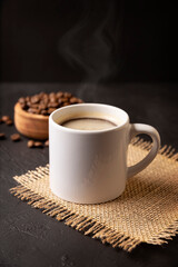 White lungo cup with hot coffee drink and toasted coffee beans scattered on a rustic black table. Close up image. Blank cup for copy space