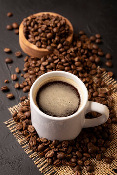 Coffee beans scattered on a rustic black table and white lungo cup with hot coffee drink. Close up image