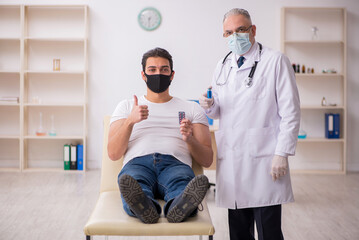 Fototapeta premium Young male patient visiting old doctor in vaccination concept