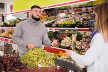 Female seller assisting customer to weigh grape. High quality photo