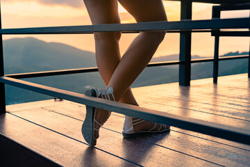 Close up of the legs of a young woman in white dress and sandals standing on a viewpoint at sunset....