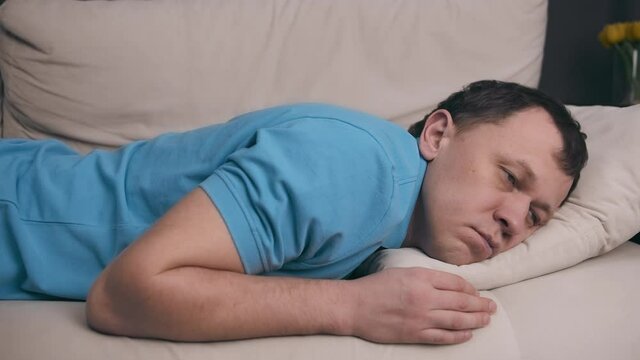 A man in a blue T-shirt collapses on the couch after a hard day