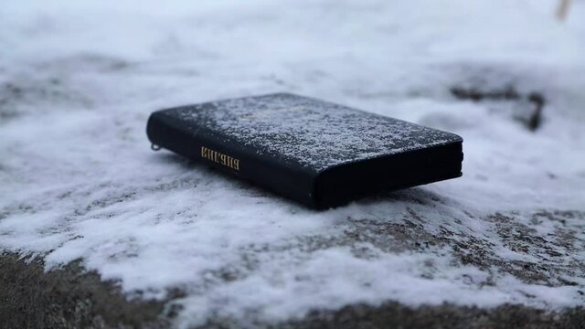 black holy bible close-up. Snow falls on the book. The Word of God for Christmas