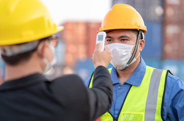 Men at work wearing face mask prevent Covid-19 infection.Manager or engineer foreman using infrared thermometer measure temperature to construction site staff worker at shipping container warehouse.