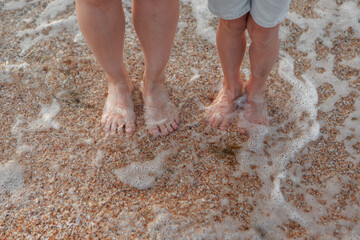 tanned legs in the sand close-up. a wave rolls onto the sand. summer vacation by the sea