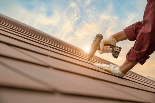 Roofer working in special protective work wear gloves, using air or  pneumatic nail gun installing concrete or CPAC cement roofing tiles on top  of the new roof under construction residential building Stock