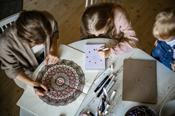 Young beautiful mother and cute daughter draw a mandala pattern together. Artistic markers and...