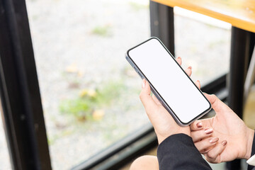 Top view mockup of a woman holding a black cell phone with the blank white screen while sitting at...