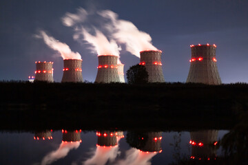 The lights of a nuclear power plant are reflected in a pond. Nuclear power plant cooling towers