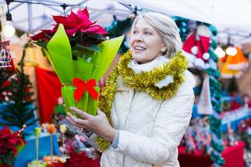 Portrait of mature woman in tinsel with Christmas flowers at fair outdoor.