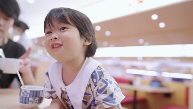 Cute asian girl having fun at restaurant dining table, happy toddler sit down on high chair, playful kid eating with kid plate set, child innocence curiosity, chidden learning age, life experiences