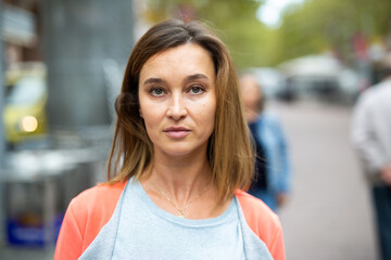 Closeup portrait of adult brown-haired woman walking along city street in warm autumn day