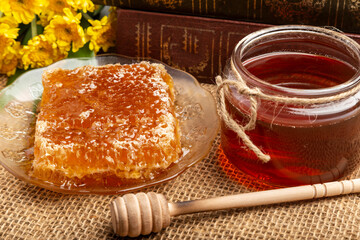 honeycomb with honey placed in a plate, a wooden dipper, a honey jar, a yellow gerbera flower. Place on hemp sackcloth