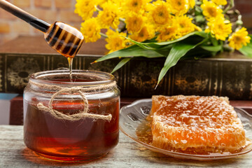 honeycomb with honey placed in a plate, a wooden dipper, a jar of honey, a yellow gerbera flower. put on old wooden planks
