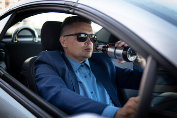 man in an expensive suit drinks beer at the wheel of a car causing the danger of an emergency. A...