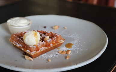 Closeup of ice cream with honey on a piece of waffle on white ceremic plate.