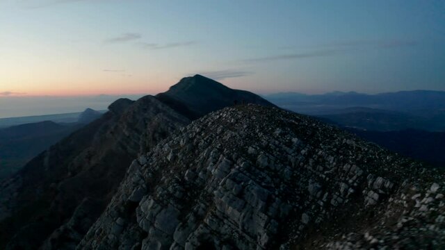 Aerial view around two men running on a rocky mountain ridge, during sunset, in Campania, Italy - orbit, drone shot