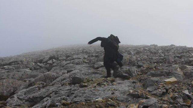 Hiker walking up a rocky mountain trail, on a foggy, autumn day, in Bulgaria - Handheld, slow motion view