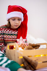 Christmas without waste. Child girl in pajamas sits on the bed and looks at toys for the tree.