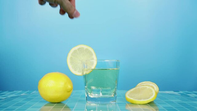 place slice fresh lemon on lemonade glass on blue tile grid table and blue background, bartender prepare fruit cocktail or fresh juice for drinking in party at bar