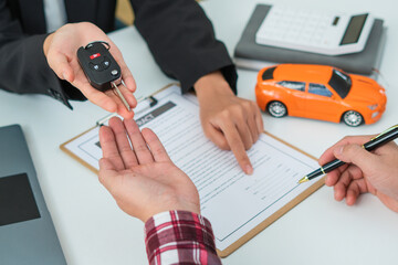 Sale agent handed over the rental car key to the customer who signed the contract and the terms of the agreement on the document, Car rental service concept.