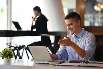 Smiling businessman having video conference with laptop computer at office desk.