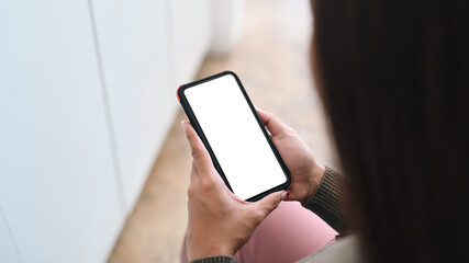 View over businesswoman shoulder holding mock up smart phone with empty display.