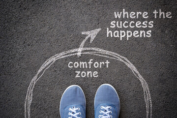 Exit from comfort zone concept. Feet in blue jeans sneakers standing inside circle and outward arrow chalky on asphalt.