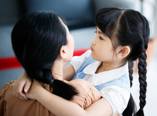 Close up shot of Asian small pretty happy preschooler girl smiling holding arms around neck hugging cuddling young lovely mother embracing love together. Mom carrying holding little child in hands