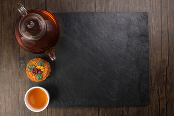 Colourful flower decorated mooncake cut slice half layer Chinese mid autumn festival on glass teapot white ceramic teacup over black slate stone border copy text space