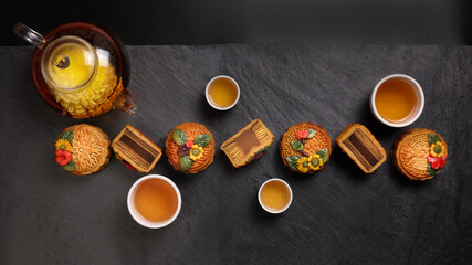 Colourful flower decorated mooncake Chinese mid autumn festival on black slate stone background small white ceramic teacup glass teapot