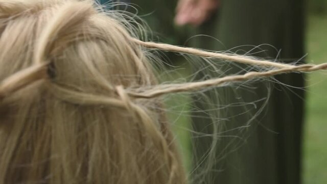 woman&rsquo;s hands braiding hair for another blond girl outside