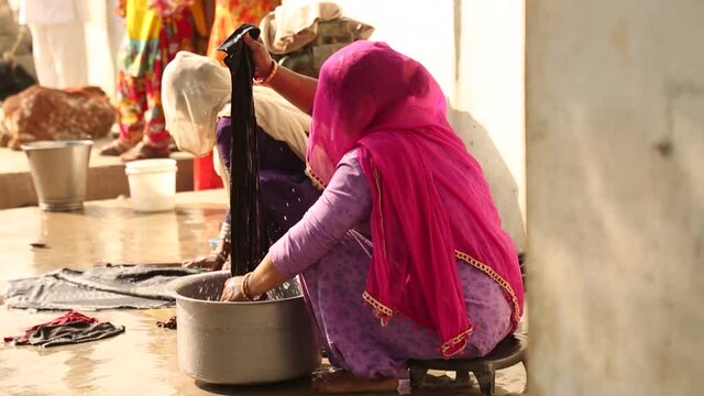 Unrecognizable Indian women with head covered by typical veil washing clothes outdoors, India. Handheld