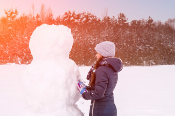 Cute girl makes a snowman on a winter day. A girl on a snow-covered field in the open air....