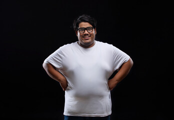 Portrait of a fat man smiling while placing hands on waist against plain background.
